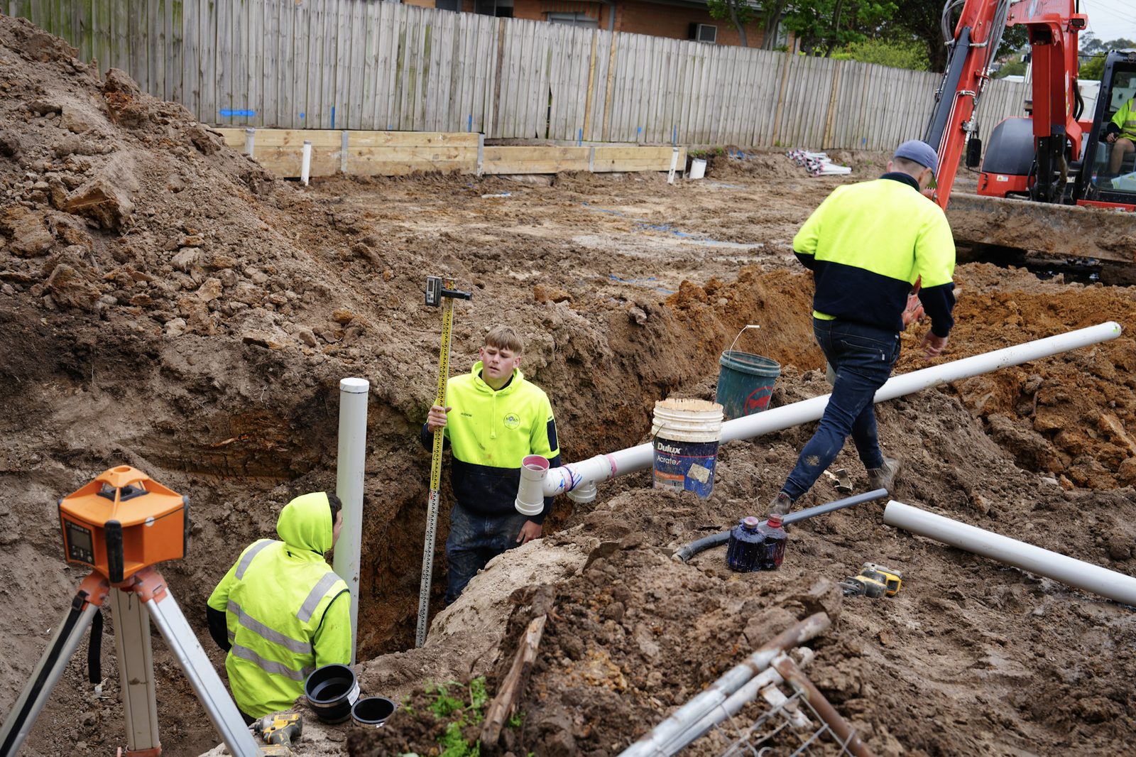 Crew in hi-vis using a laser level to set drainage falls in a trench.