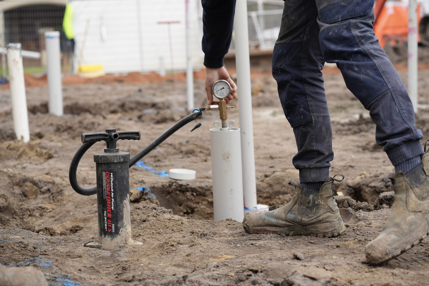 Crew installing white PVC stormwater risers along a trench.